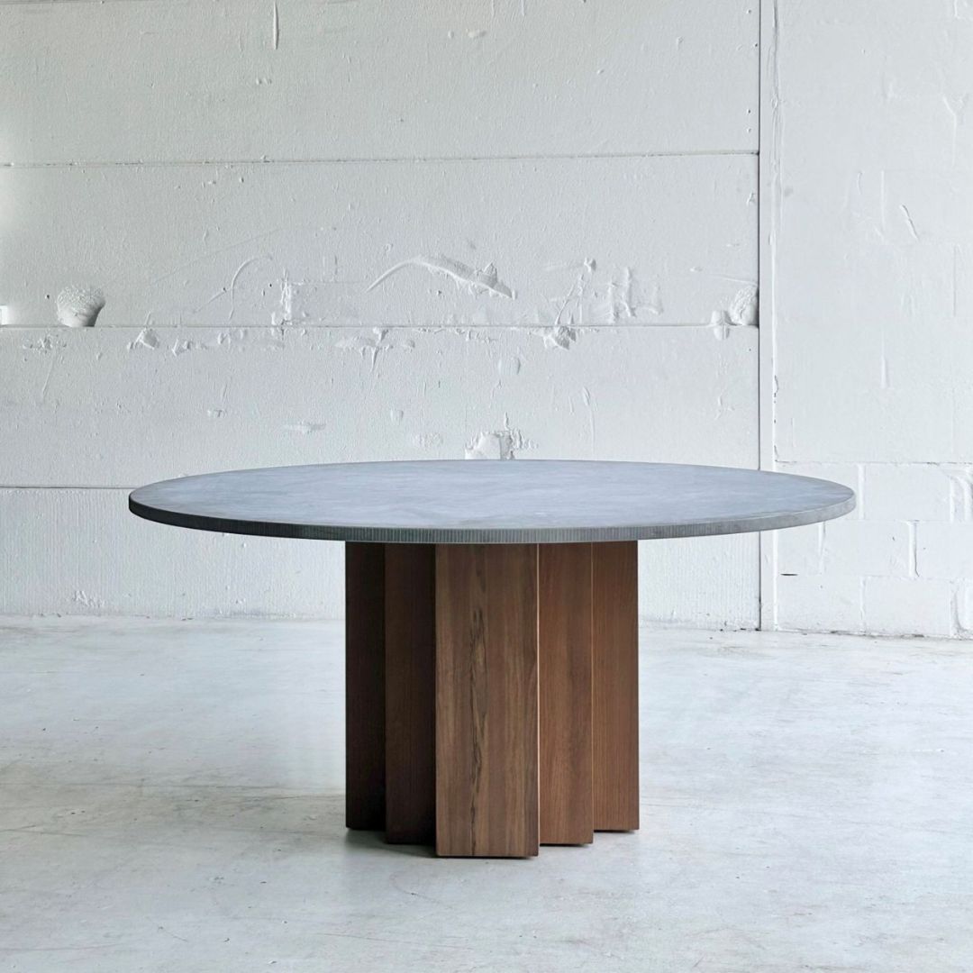 Round dining table with marble top and wooden legs against a white wall.